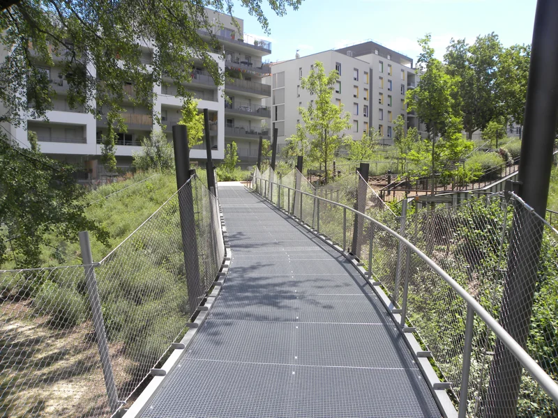 Passerelle piétonne en caillebotis métallique dans un parc